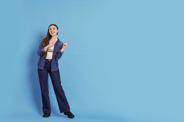 Poster - Smiling woman in stylish jeans pointing at something on light blue background. Space for text