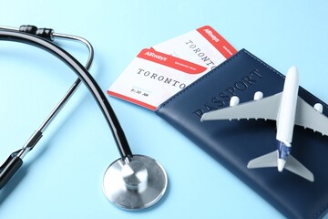 Wall Mural - Medical tourism. Stethoscope, plane model, passport and flight tickets on light blue background, closeup