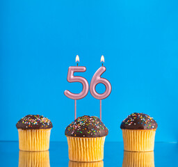 Wall Mural - Three birthday cupcakes with number 56 candle - Blue background.