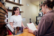 © Miguel Lifestyle - Barista smiling at customer reading menu in coffee shop