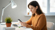 © Postmodern Studio - A woman is sitting at a desk with a laptop and a cell phone