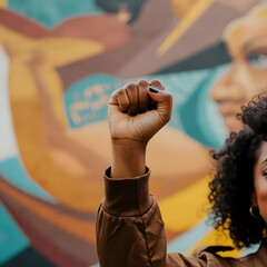 Raised fist of protester in front of colorful mural representing equality and social justice movement