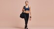 © schiers_images - Fit woman in athletic gear holding a sports bag and water bottle, symbolizing health, fitness, and active lifestyle. Neutral backdrop enhances focus on the subject's physical fitness and commitment.
