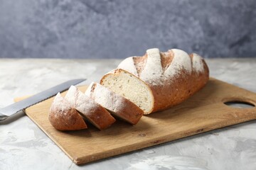 Wall Mural - Wooden cutting board with fresh bread and knife on grey table, closeup