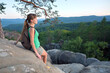 © bilanol - Sportive female hiker sitting alone taking a break on hillside trail. Lonely woman enjoying view of evening nature from rocky cliff on wilderness path. Active lifestyle concept