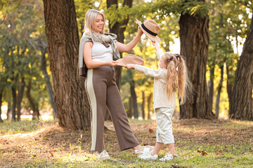 Poster - Little girl and her mother with hats in park on autumn day