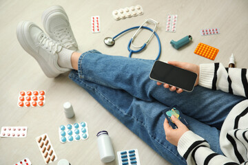 Wall Mural - Woman with modern mobile phone, credit card, different pills and medical supplies sitting on light floor