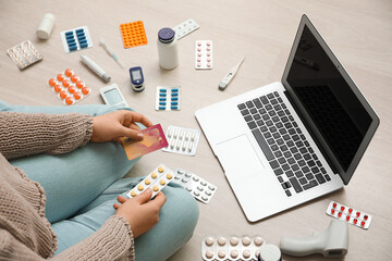 Wall Mural - Young woman with credit card, different medicines, medical supplies and modern laptop sitting on light floor