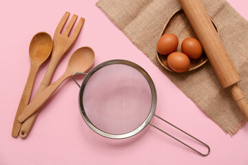 Wall Mural - Metal sieve, wooden kitchen utensils and chicken eggs on pink background