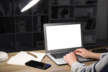 Wall Mural - Woman with modern laptop, mobile phone, notebook and pen working at wooden table in evening