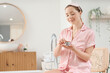 © Pixel-Shot - Young woman applying cream on her face in bathroom
