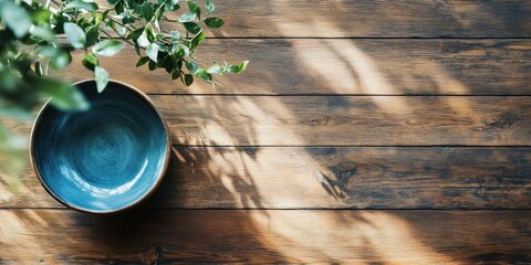 Fototapete - Artistic blue bowl on rustic wooden tabletop with green foliage casting shadows left and ample copy space in top right corner for text
