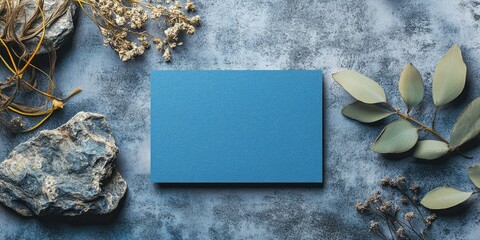 Aufkleber - Blue rectangular card centered on a textured gray background surrounded by dried flowers, rocks, and green leaves creating an earthy and tranquil aesthetic.