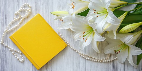 Poster - Yellow book on wooden surface next to white lilies and pearl necklace, green leaves surrounding flowers, creating a serene flat lay composition.