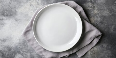 Poster - Minimalistic top view of a white plate resting on a soft grey napkin with subdued tones creating a calm and elegant setting for dining.