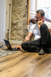 © simona - The man sits alone on the floor in a chalet, using his laptop to surf the internet and browse social media, enjoying a peaceful moment of relaxation while on a vacation in the mountains, disconnected