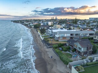 Coastal townhouses line a beach at dusk. People stroll along the sand. Tranquil seaside scene. MILFORD, AUCKLAND, NEW ZEALAND