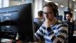© RSATRIA - Focused worker wearing headphones on computer in busy office