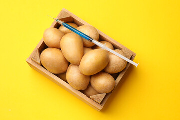 Wall Mural - GMO concept. Potatoes and syringe with liquid in crate on yellow background, top view