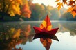 © wichit - A crimson paper boat adorned with autumn leaves serenely floats on a tranquil pond, mirroring the vibrant hues of the surrounding fall foliage.