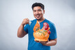 © Daniel - An Asian man in a blue t-shirt smiling while holding a ceramic rooster piggy bank in one hand and inserting a bill with the other. The background is isolated and pure white