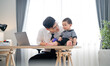 © Hip.hub - Father playing with baby at home workstation during daytime while working remotely in a modern and cozy environment