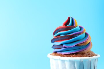 Wall Mural - One delicious cupcake with colorful cream on light blue background, closeup. Space for text