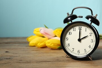 Poster - Spring time. Alarm clock and beautiful tulips on wooden table against light blue background, space for text