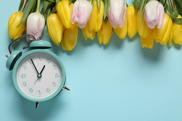 Poster - Spring time. Alarm clock and beautiful tulips on light blue background, flat lay. Space for text