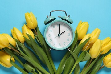 Poster - Spring time. Alarm clock and beautiful tulips on light blue background, flat lay