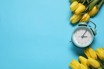 Poster - Spring time. Alarm clock and beautiful tulips on light blue background, flat lay. Space for text