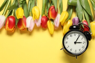 Poster - Spring time. Alarm clock and beautiful tulips on yellow background, flat lay. Space for text