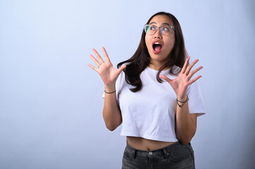 A young Asian woman with glasses and long dark hair, wearing a white crop top, makes a surprised expression with both hands raised near her face against a plain white background.