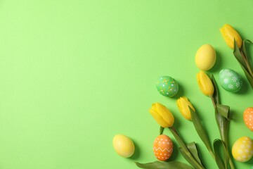 Wall Mural - Easter eggs and beautiful tulips on green background, flat lay. Space for text