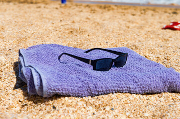 A pair of sunglasses and a towel are laying on the sand