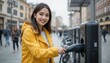 © Pavel Lysenko - A cheerful young woman in a vibrant yellow jacket connects her electric vehicle to a charger in a bustling city. Bystanders stroll by, adding to the lively atmosphere