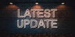 © Rodrigo - Warm-toned neon 'LATEST UPDATE' sign on a dark brick wall, illuminated by vintage wall lamps.