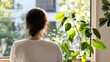 © Iona - A person seated near a window, enjoying warm sunlight filtering through, surrounded by fresh indoor plants creating a serene and reflective mood.