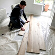 © lina - male worker carefully installing light-colored wood flooring in a home.