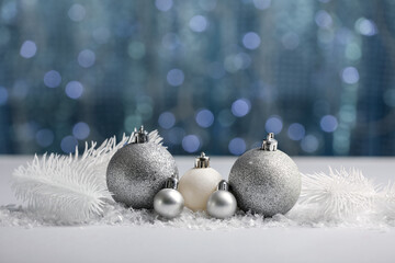 Wall Mural - Christmas balls with snow and fir tree branches on table against blurred lights