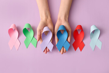 Wall Mural - Female hands with different paper ribbons on lilac background, closeup. World Cancer Day