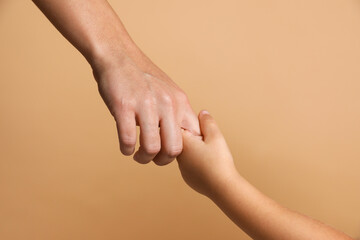 Wall Mural - Mother and child holding hands on beige background, closeup