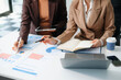 © laddawan - Two young business women sitting at table.colleagues working together, have a discussion and using tablet
