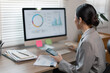 © David - Asian business finance market analyst holdind phone working at office .Business woman analyze document Graphs and diagramm on Desktop Computer screen.