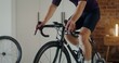© m-art - A young athletic man trains on a bike simulator, practicing standing up riding. Indoor cycling in a modern home interior
