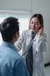 © Phimwilai - Young asian female doctor wearing a lab coat, using a stethoscope to examine a male patient in a hospital room during a medical appointment, providing attentive care and consultation