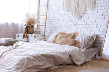 Canvas Print - Cozy bedroom with interior design in boho style, bed mattress on floor, cushions, frame poster, home decor, stepladder, macrame panel against white brick wall. Concept of classy house and apartment.	
