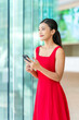 © StockPhotoRepublic - Young Asian Woman in Red Dress Using Phone Indoor a Modern Office Building