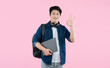 © STOCK88PHOTOGRAPHER - Portrait of Asian male student wearing backpack and headphones, holding laptop, nice gesture on pink background