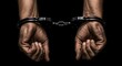 © ufuk - Close-Up of Man’s Hands in Metal Handcuffs, Tense Expression, Dramatic Black Background.